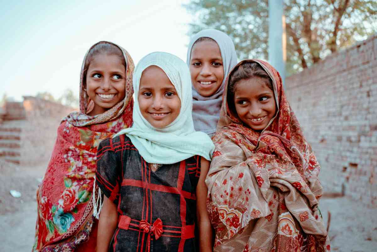 Four smiling girls standing together, the kind of everyday community daily sadaqah reaches